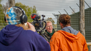 Noah's Ark Zoo Farm CEO, Larry Bush, being filmed by two crew members in front of an animal enclosure. Film Camera on on a tripod with boom on top. 