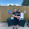 Katie Cox, local fundraiser,  holds her son in front of a wooden board and table during her fundraising challenge. 