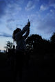 Female staff members observe bat monitoring technology as she holds it towards sky in the dark.
