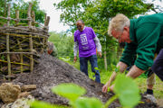 Man digs dirt in green uniform, in the background a man from Ripple Effect in a purple t-shirt observes the work