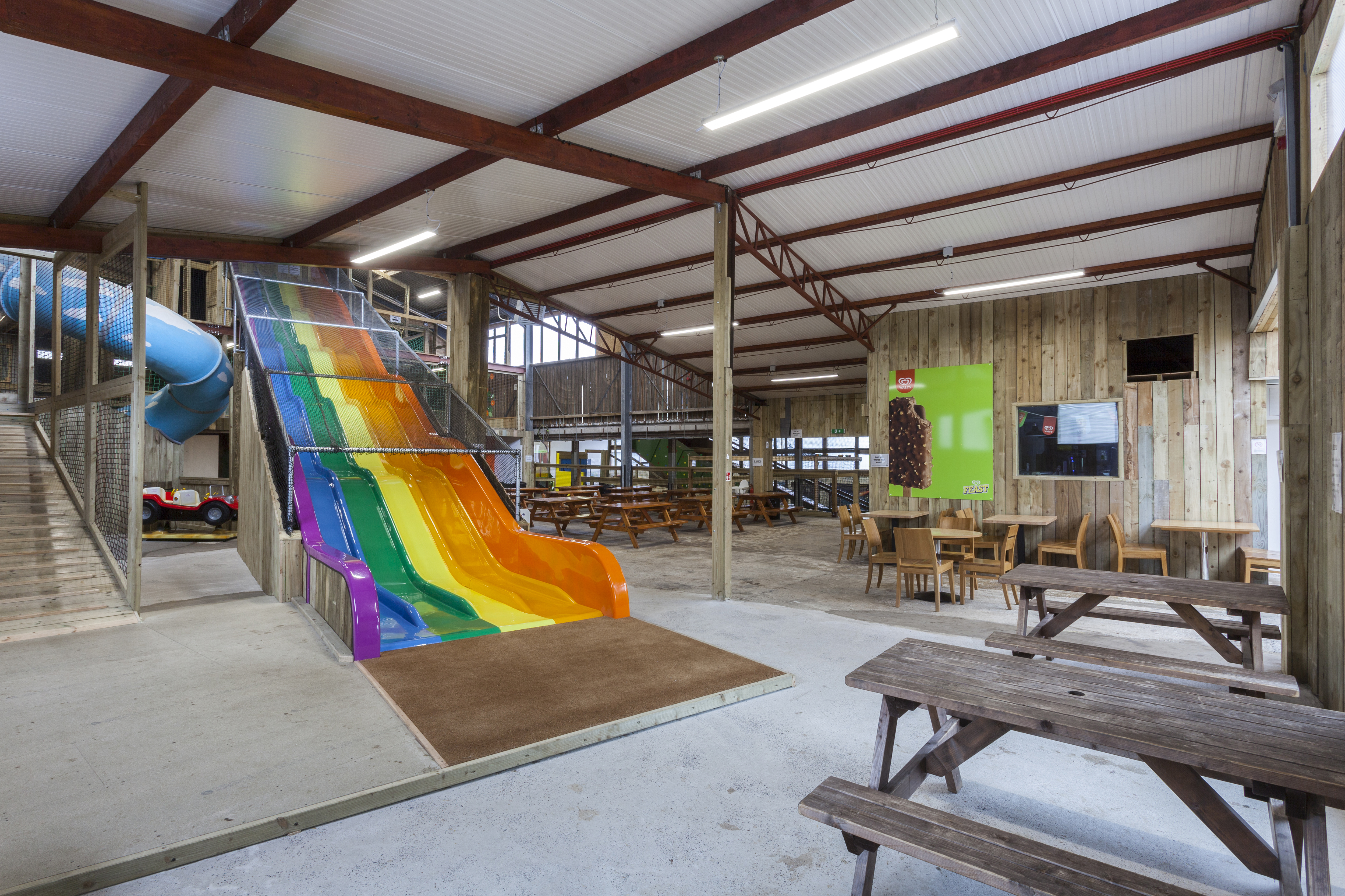 Photo showing a long rainbow slide in an indoor play area with eco friendly lighting and picnic benches