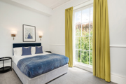 A luxurious hotel room with yellow floor length curtains and a large double bed. 