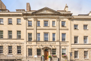 Front of the Berkeley Square Hotel, a sand coloured impressive building with a large wooden door. 