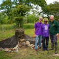 3 members of staff stand next to keyhole garden in woodland area