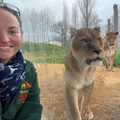 Keeper Emily smiles in front of glass with two African Lions