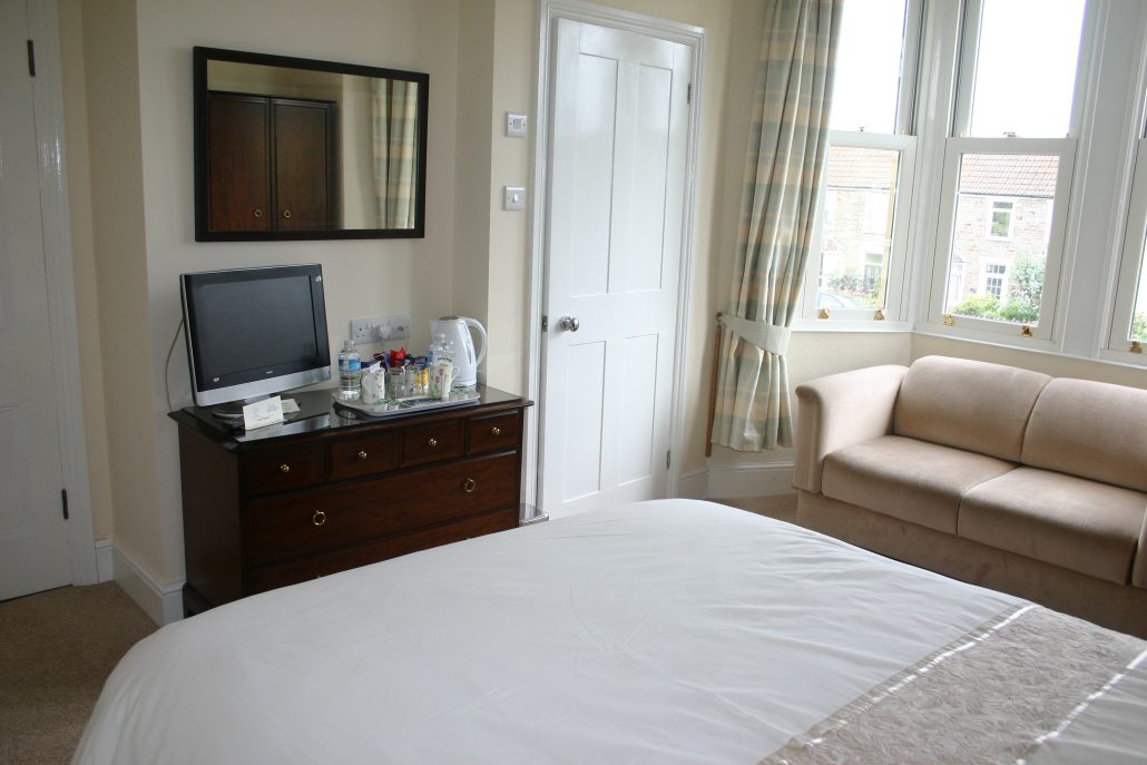 A hotel room with a double bed, TV on a dark unit and a sofa