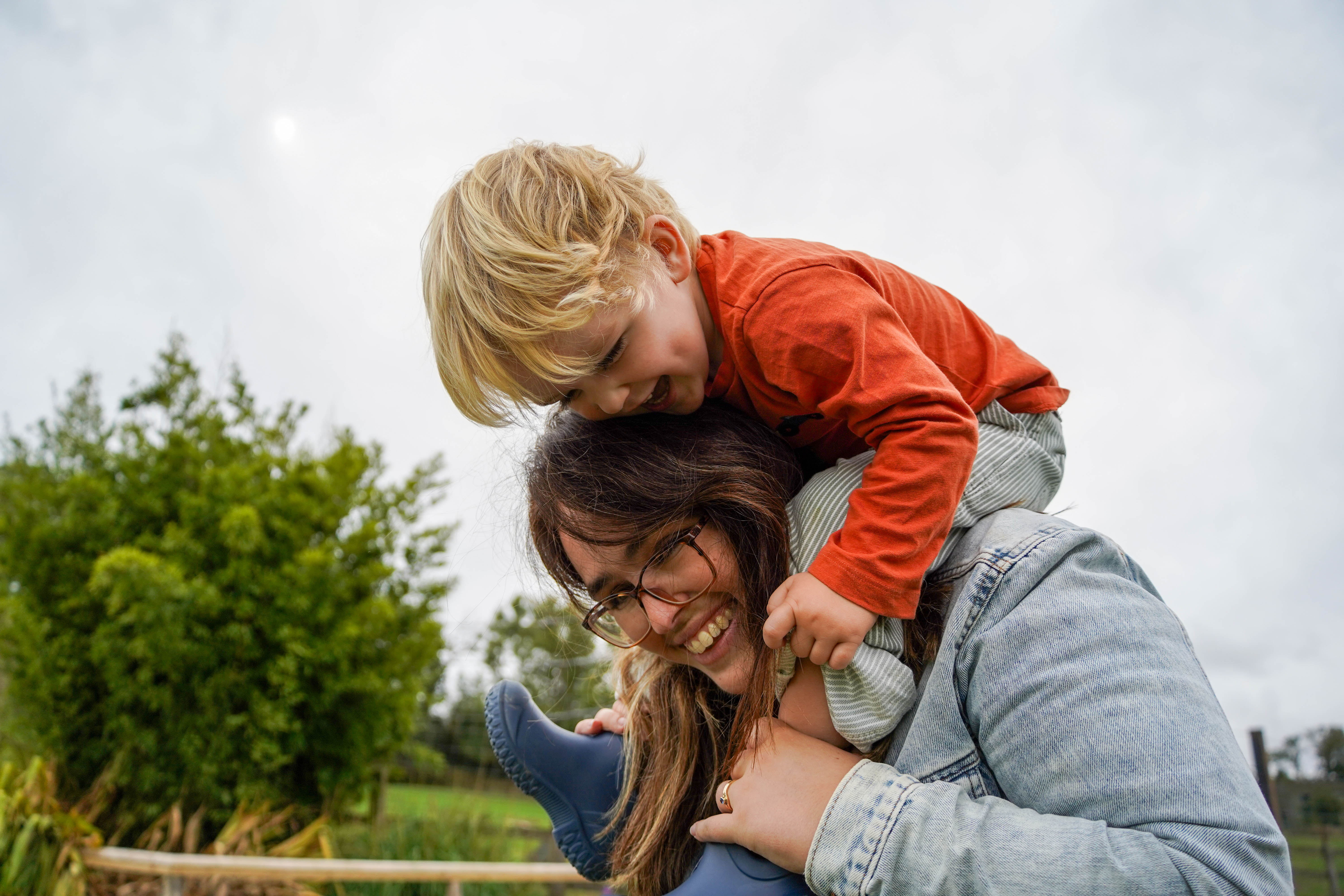 Toddler sits on his mums shoulders laughing as they walk through the zoo. 