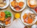 A selection of white plates, with various breakfast items on them, a glass of orange juice and a breakfast menu. 