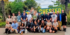 Large group of people, stood in front of Chester Zoo entrance sign. 
