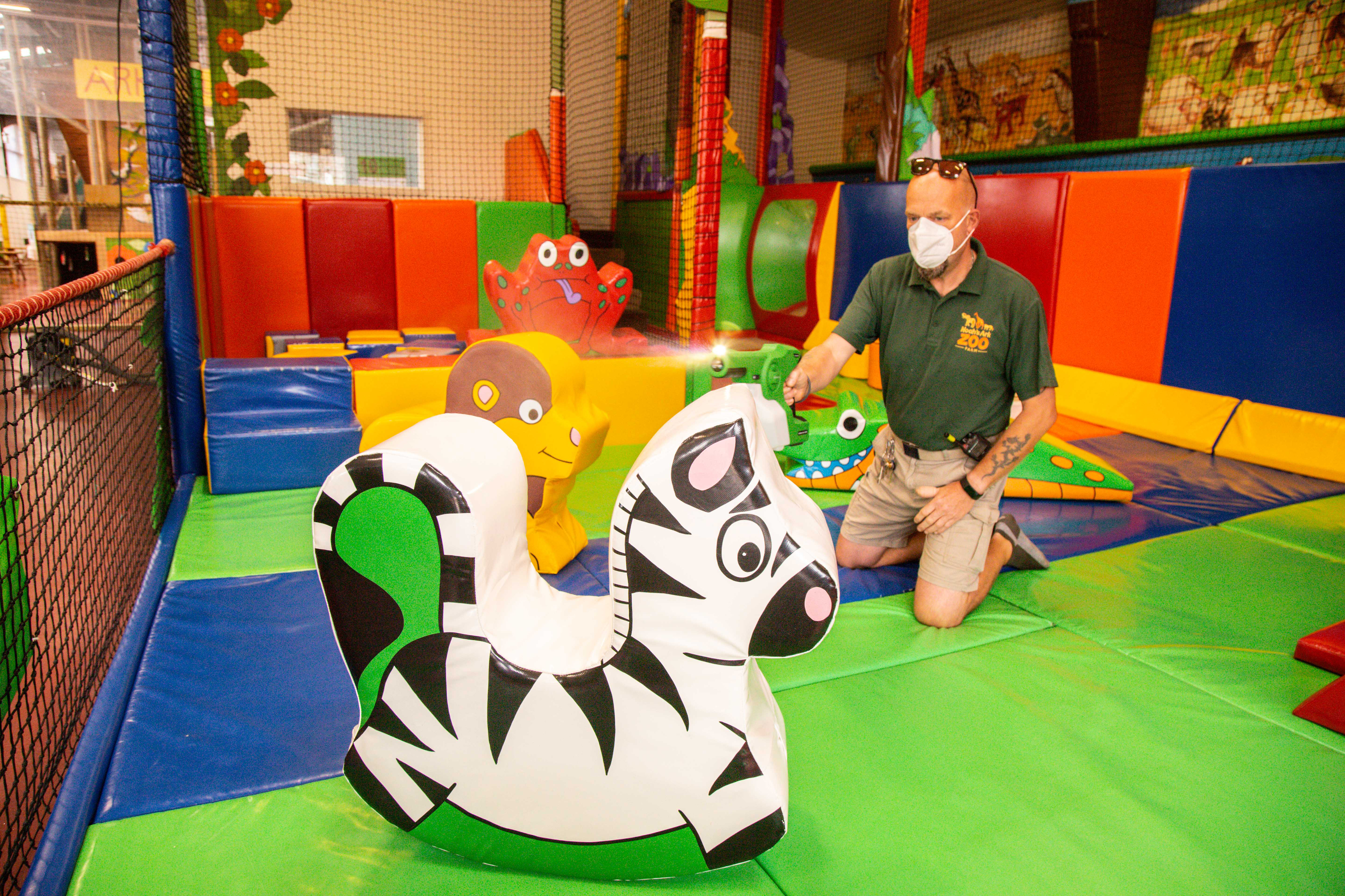 Man wearing a facemask cleans soft play zebra shape using a misting spray