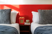 Luxurious twin beds against an orange wall with a radio and cup of tea and a book on a table between the beds. 